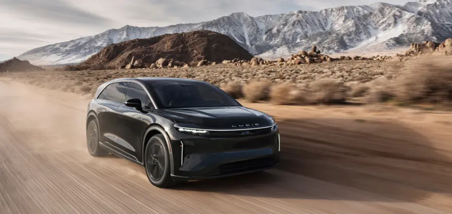 A Lucid Gravity driving down a desert road with mountains in the background.