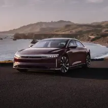 A Zenith red metallic Lucid Air Grand Touring driving along a bay.