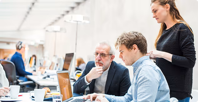 Three coworkers collaborating around a laptop in a bright modern office.