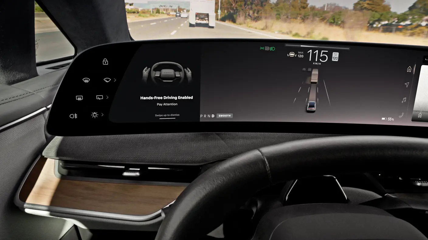 Écran du tableau de bord de la voiture affichant « Conduite mains libres activée » à 115 km/h sur une autoroute.