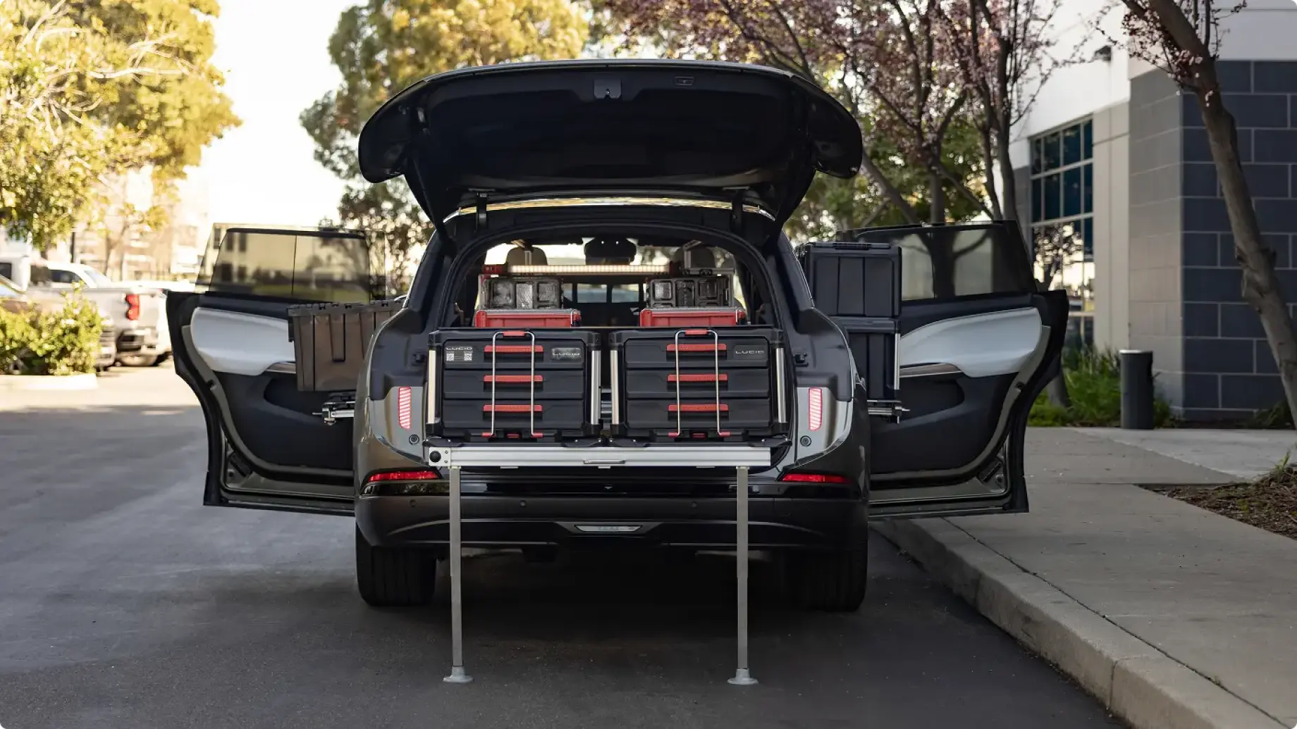 Lucid Gravity SUV with open rear hatch, loaded with black and red storage cases on a sliding cargo platform with support legs.