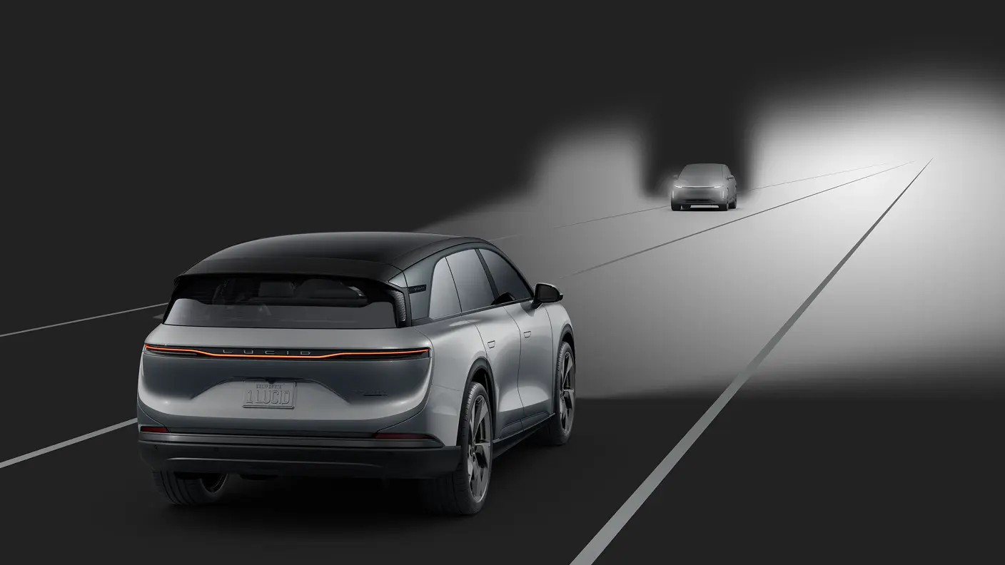 Rear view of a silver Lucid electric SUV on a dark road, with headlights illuminating a car ahead at night.