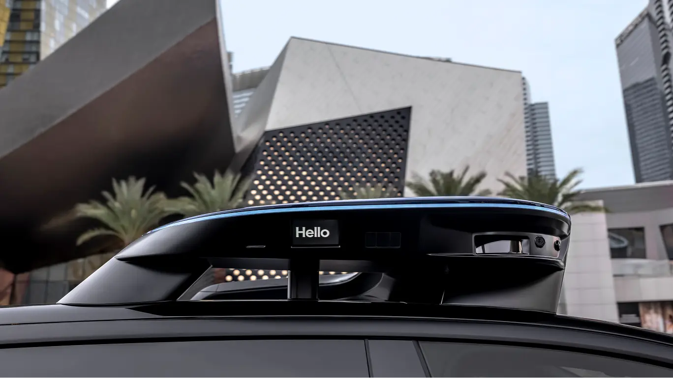 Black car sensor unit displaying "Hello" in front of modern architectural building with palm trees and city skyline.