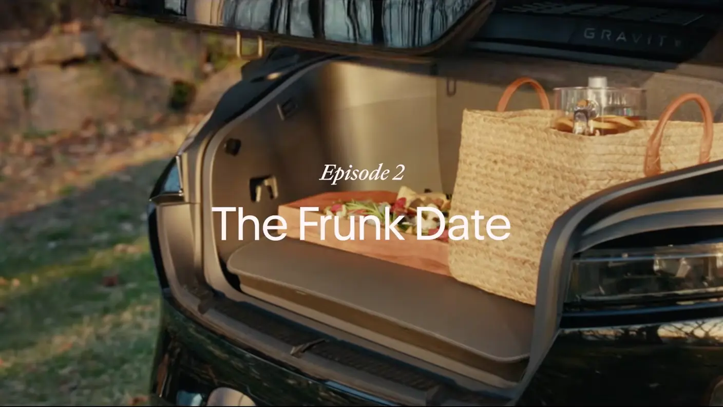 Open frunk of a dark SUV holding a picnic basket and cutting board, with text reading "Episode 2: The Frunk Date."