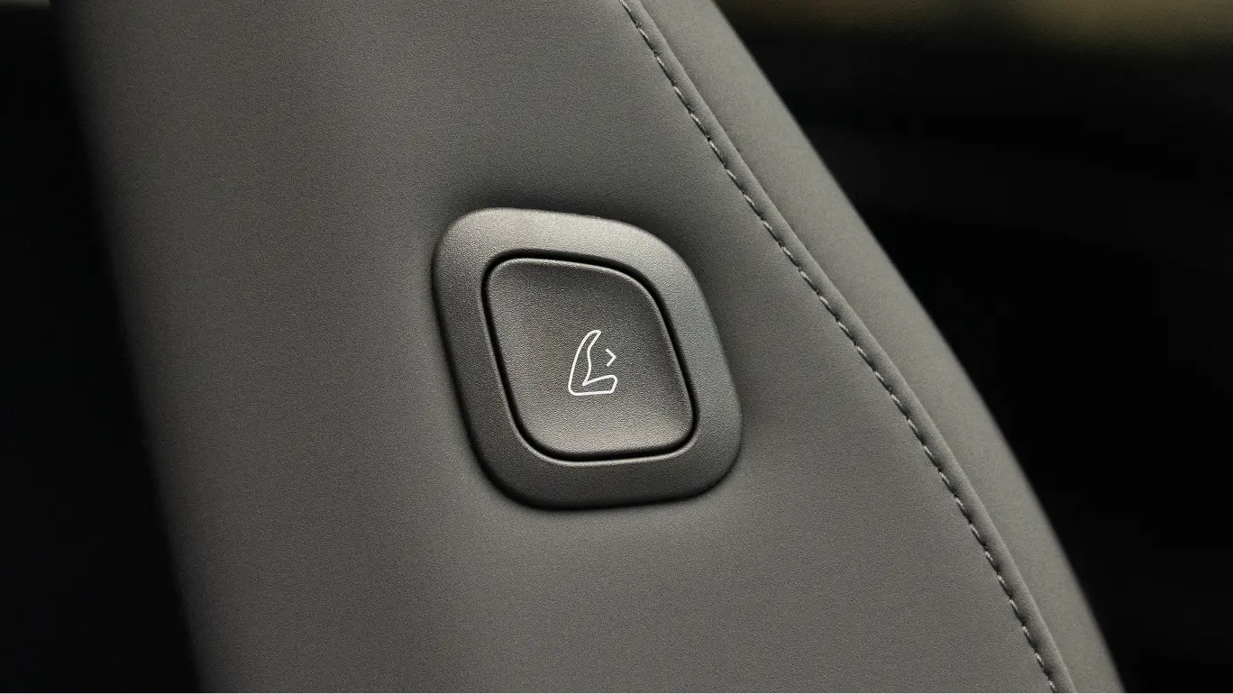 Gray leather car seat with a square button featuring a seat folding icon, part of vehicle's interior controls.