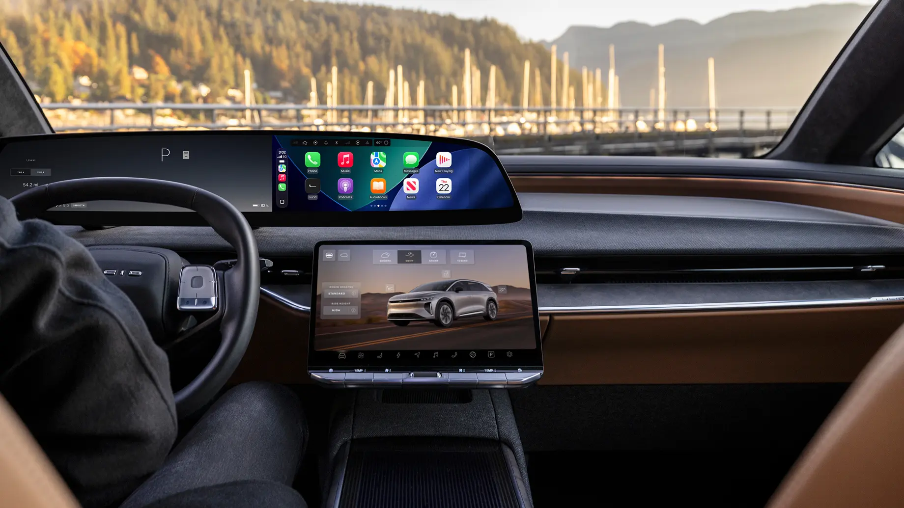 Luxury electric car interior with dual touchscreens showing CarPlay and vehicle settings, tan leather trim, and a marina view.
