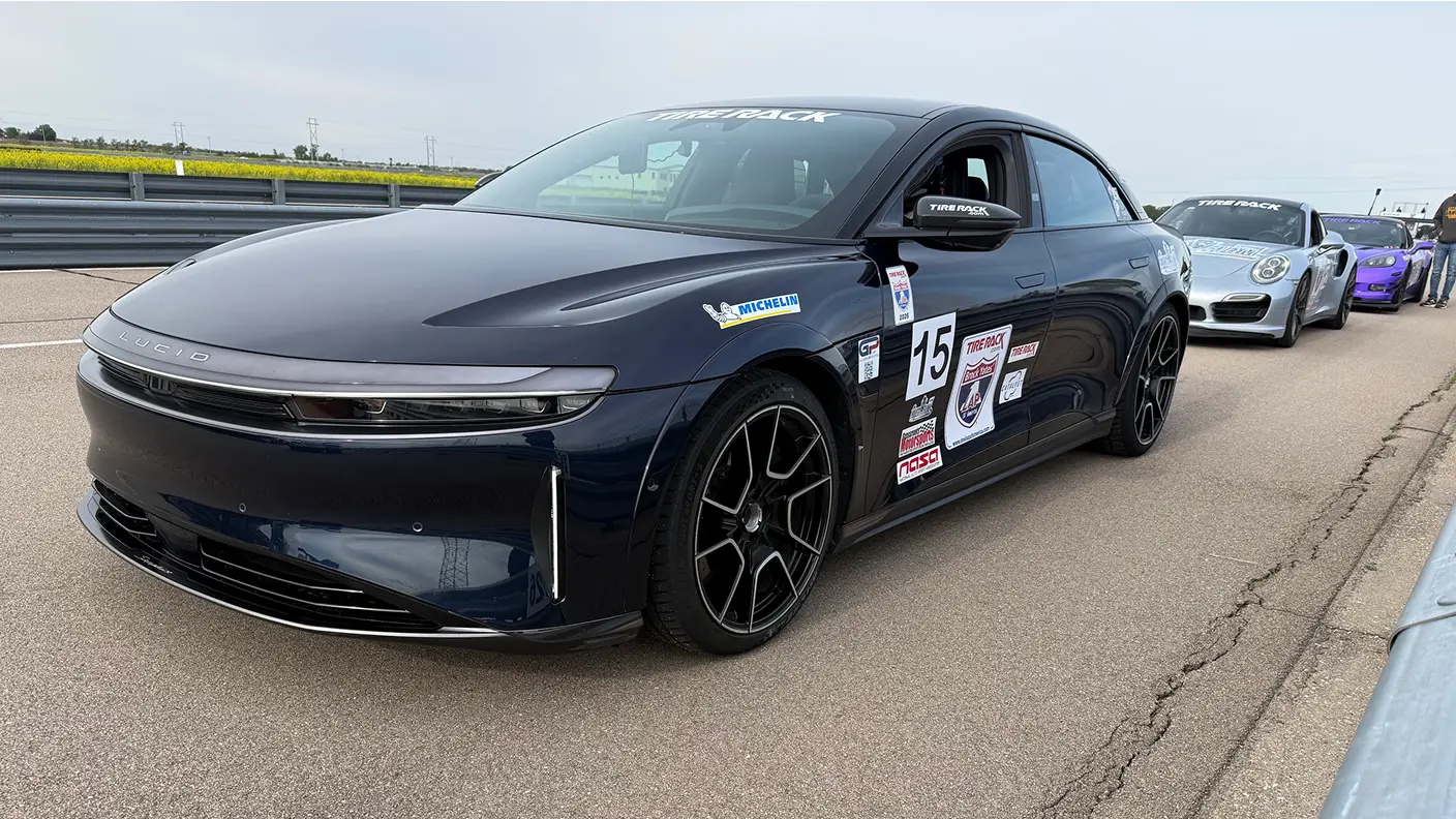 Lucid Air Sapphire sedan with race number 15 and sponsor decals on a track, with other cars lined up behind it.